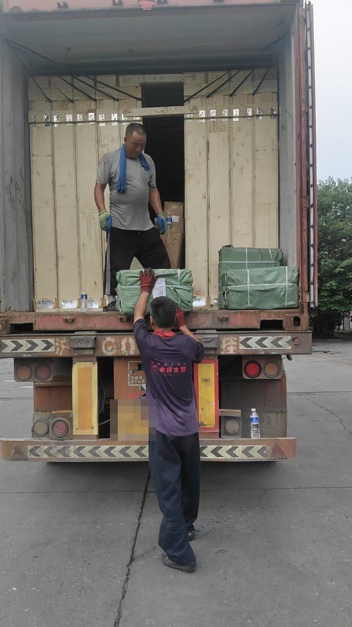 Two workers loading green-wrapped cargo into a container